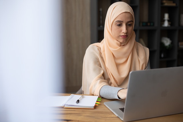 A landlord in a peach hijab sits at a desk and types a property listing