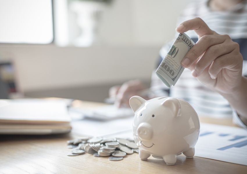 person placing money into a white piggy bank